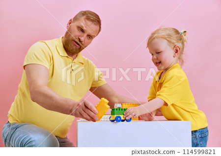 Playtime construction fun. Dad and his daughter share playful bonding activity, assembling colorful toy-blocks against pink studio background. 114599821
