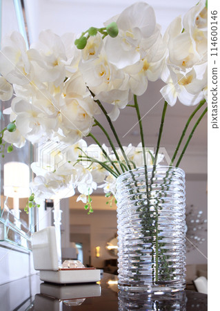 Flowers in a glass vase. A bouquet of white orchids in the interior. A vase with beautiful orchid flowers on the dresser in the living room. Flowers in a glass vase. A bouquet of white orchids in the interior. A vase with beautiful orchid flowers on the dresser in the living room. 114600146