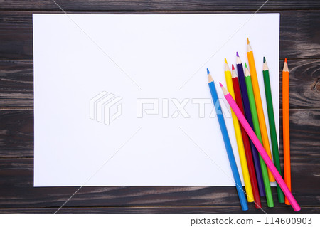 Many different colored pencils with white paper on brown wooden background Many different colored pencils with white paper on brown wooden background 114600903