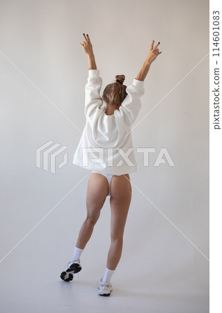 Blonde girl in a hoodie and panties posing with her back on a white background 114601083