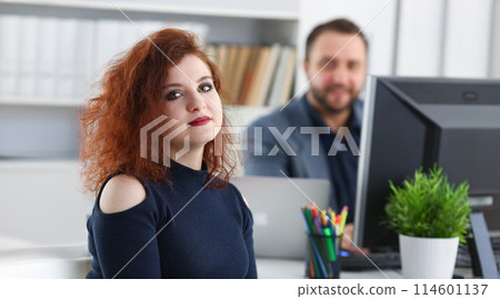 young beautiful red haired woman sit at table in office in cabinet of her boss 114601137