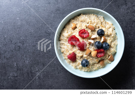 Oatmeal porridge with raspberries, blueberries and almonds in bowl on black background. Top view Oatmeal porridge with raspberries, blueberries and almonds in bowl on black background. Top view 114601299