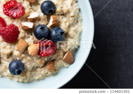 Oatmeal porridge with raspberries, blueberries and almonds in bowl on black background. Top view 114601301