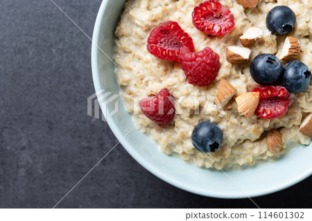 Oatmeal porridge with raspberries, blueberries and almonds in bowl on black background. Top view 114601302