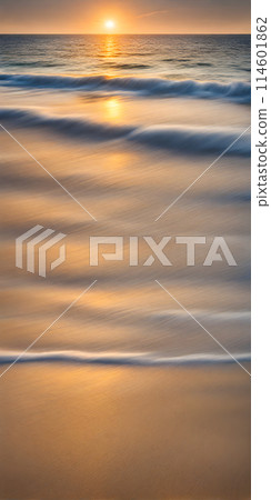 Smoothly blurred sky over a sun-kissed calm sea, golden sands of a tranquil beach in the foreground 114601862