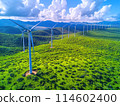Wind farm with multiple turbines set against a lush green landscape under a clear blue sky with scattered clouds 114602400