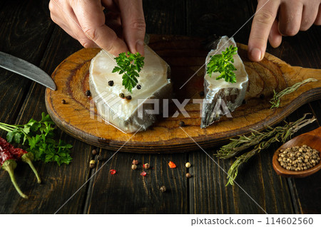 Close-up of a chef hands adding aromatic parsley to Anarhichas fish before frying. The concept of a delicious fish diet in a restaurant Close-up of a chef hands adding aromatic parsley to Anarhichas fish before frying. The concept of a delicious fish diet in a restaurant 114602560