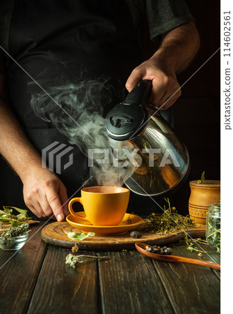 A man adds boiling water to a mug to make medicinal tea in the kitchen. Traditional medicine concept or making healthy tea from medicinal dry plants 114602561
