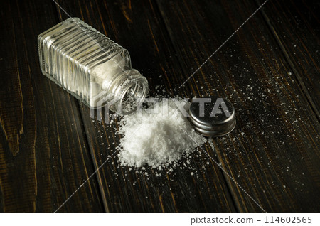 A pile of salt from a salt shaker on a black table. Concept of excessive salt consumption, which may be the cause of diabetes or other diseases A pile of salt from a salt shaker on a black table. Concept of excessive salt consumption, which may be the cause of diabetes or other diseases 114602565
