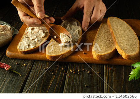 A quick meal is prepared by the hands of a chef using lard and sliced rye bread on a kitchen board. Advertising space on a dark background 114602566