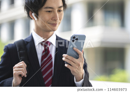 Hands of a businessman wearing earphones holding a smartphone Hands of a businessman wearing earphones holding a smartphone 114603973