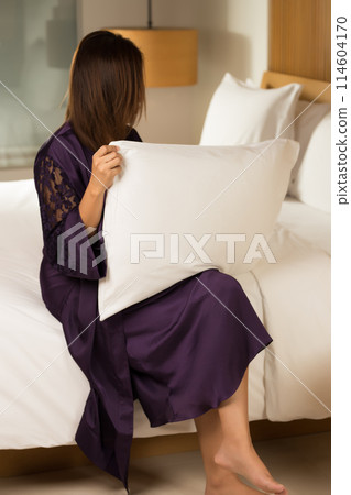 A woman in an elegant robe enjoys the soft comfort of a pillow. A woman in an elegant robe enjoys the soft comfort of a pillow. 114604170