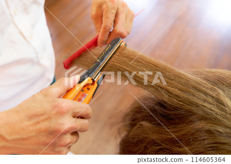 Stylist using a hair iron Stylist using a hair iron 114605364
