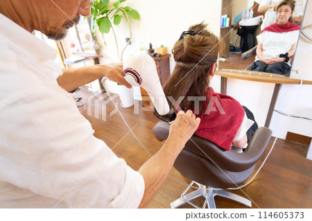 A male stylist drying hair with a hairdryer and an elderly female customer 114605373