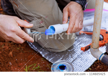 An experienced plumber seals pvc plastic pipes with glue before gluing them together 114605425