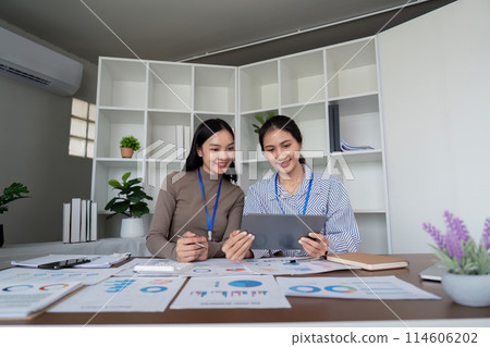 Two Asian women collaborating on a project in a modern office. Concept of teamwork, business, and productivity Two Asian women collaborating on a project in a modern office. Concept of teamwork, business, and productivity 114606202