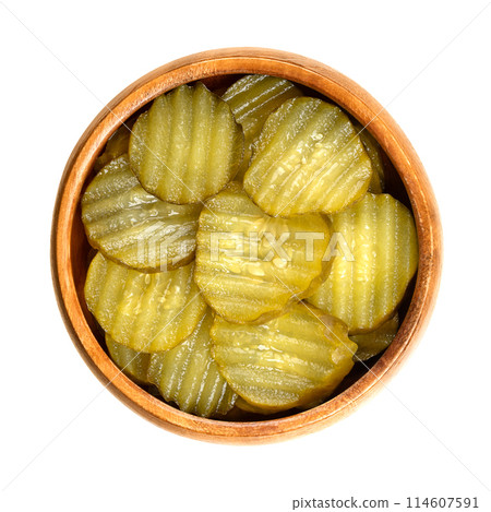 Burger gherkin slices, in a wooden bowl. Pickled cucumbers, cut in round and wavy form, pasteurized and preserved in vinegar brine, with spices. Barbecue side dish and ingredient between bun halves. 114607591