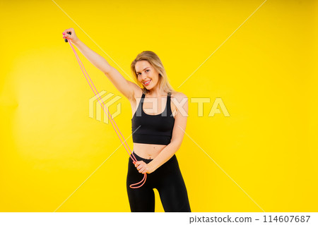 Blond woman with jump rope in studio, yellow red and dark background 114607687