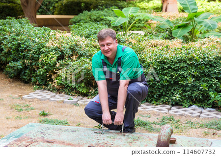 A working plumber opens a heavy hatch to access a pipe A working plumber opens a heavy hatch to access a pipe 114607732