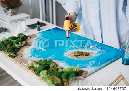 Artist Perfecting Epoxy Resin Coastal Scene with hand burner 114607767