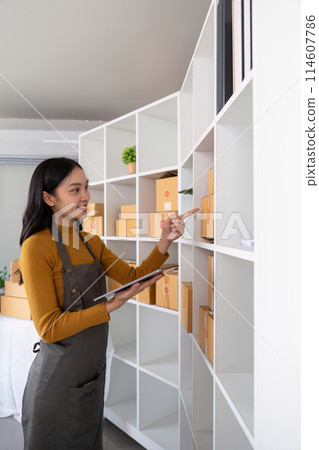 Ecommerce business owner managing inventory and checking stock in home office. Small business entrepreneur organizing packages for shipment and using a tablet for inventory tracking Ecommerce business owner managing inventory and checking stock in home office. Small business entrepreneur organizing packages for shipment and using a tablet for inventory tracking 114607786