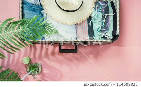 Open suitcase with female clothes, leaf of fern, freshness detox beverage on pink. Top view with copy space. Summer travel concept. 114608823