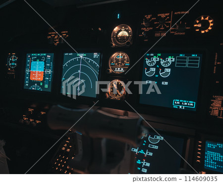 Cockpit view of an airplane during a night-time flight with illuminated instrument panels Cockpit view of an airplane during a night-time flight with illuminated instrument panels 114609035