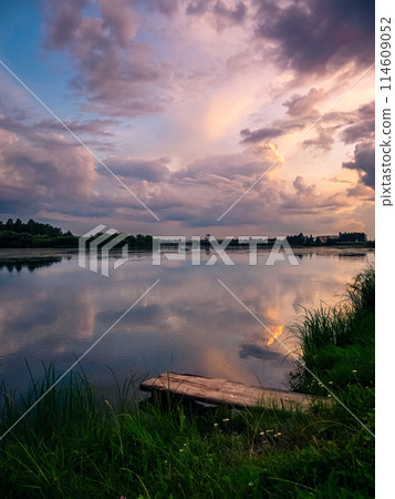 Beautiful pink sunset over calm lake at countryside evening. Tranquil lake with a wooden dock in the foreground. Beautiful pink sunset over calm lake at countryside evening. Tranquil lake with a wooden dock in the foreground. 114609052