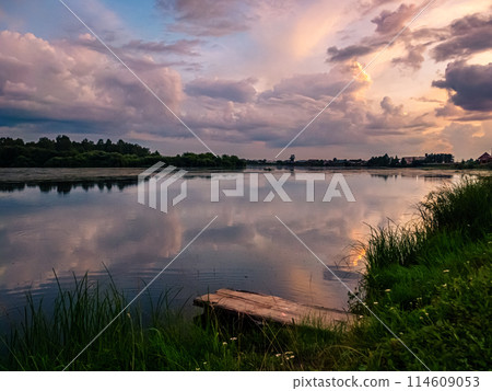 Beautiful pink sunset over calm lake at countryside evening. Tranquil lake with a wooden dock in the foreground. 114609053