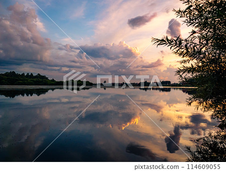 Calm river at sunset with reflective sky in rural countryside landscape Calm river at sunset with reflective sky in rural countryside landscape 114609055