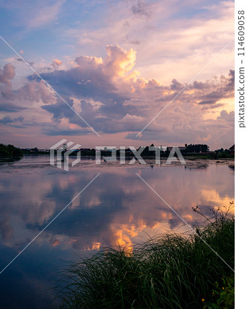 Calm river at sunset with reflective sky in rural countryside landscape 114609058