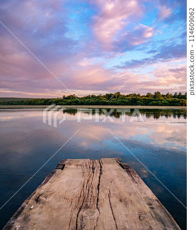 Beautiful pink sunset over calm lake at countryside evening. Tranquil lake with a wooden dock in the foreground. Beautiful pink sunset over calm lake at countryside evening. Tranquil lake with a wooden dock in the foreground. 114609062