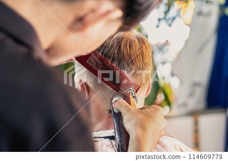 Neat young Vietnamese hairdresser makes haircut to male. Back view. Professional skills 114609778