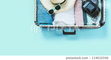 Open suitcase with female clothes for trip on pastel blue background. Top view with copy space. Summer concept travel. 114610340