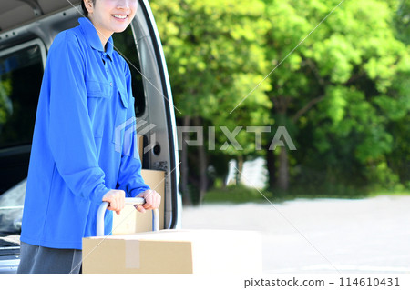 A female delivery driver carrying packages on a trolley outside A female delivery driver carrying packages on a trolley outside 114610431