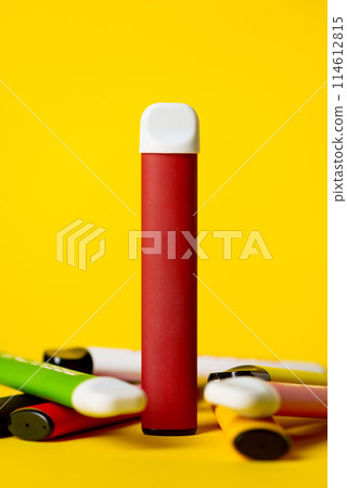 Colorful disposable electronic cigarettes on a yellow background. The concept of modern smoking, vaping and nicotine. 114612815
