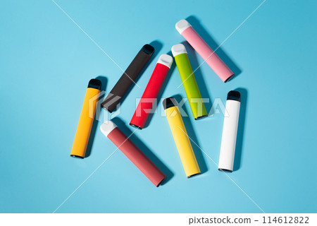 Layout of colorful disposable electronic cigarettes with shadows on a blue background. The concept of modern smoking, vaping and nicotine. Top view Layout of colorful disposable electronic cigarettes with shadows on a blue background. The concept of modern smoking, vaping and nicotine. Top view 114612822