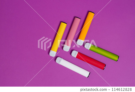 Colorful disposable electronic cigarettes on a purple background. The concept of modern smoking, vaping and nicotine. Top view. Colorful disposable electronic cigarettes on a purple background. The concept of modern smoking, vaping and nicotine. Top view. 114612828