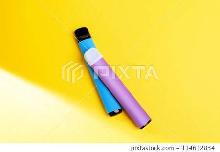 disposable electronic cigarettes with shadow on a yellow background with copy space. The concept of modern smoking, vaping and nicotine. top view. disposable electronic cigarettes with shadow on a yellow background with copy space. The concept of modern smoking, vaping and nicotine. top view. 114612834