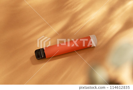 orange stick - disposable vaping device, electronic cigarette on a beige background. Flat lay, top view, minimal design with shadows of sunlight. 114612835