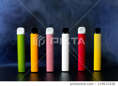 Set of colorful disposable electronic cigarettes on a black background with smoke. The concept of modern smoking, vaping and nicotine. 114612836
