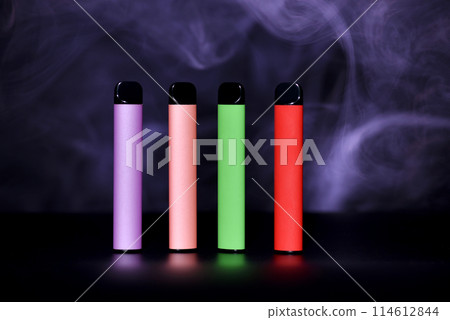 Set of colorful disposable electronic cigarettes on a black background with colour smoke. The concept of modern smoking, vaping and nicotine. Set of colorful disposable electronic cigarettes on a black background with colour smoke. The concept of modern smoking, vaping and nicotine. 114612844