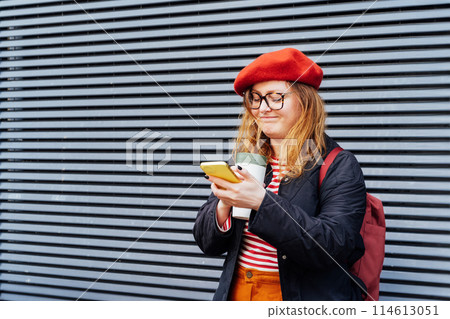 Young smiling plus size woman with backpack using mobile phone, drinking coffee outdoors on the street. Confident fashion hipster messaging, chatting, working remotely. Using navigator app for travel Young smiling plus size woman with backpack using mobile phone, drinking coffee outdoors on the street. Confident fashion hipster messaging, chatting, working remotely. Using navigator app for travel 114613051