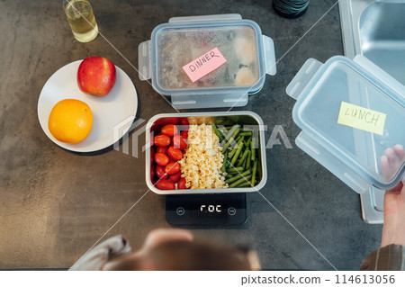 Healthy diet plan for weight loss, daily ready meal menu. Close up Woman weighing lunch box cooked in advance,ready to eat on kitchen scale. Balanced portion with healthy dish. Pre-cooking concept Healthy diet plan for weight loss, daily ready meal menu. Close up Woman weighing lunch box cooked in advance,ready to eat on kitchen scale. Balanced portion with healthy dish. Pre-cooking concept 114613056