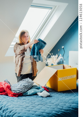 Woman selecting clothes from her wardrobe for recycling, donating to a Charity shop. Decluttering, Sorting clothes, Cleaning Up. Reuse, second hand concept. Conscious consumer, sustainable lifestyle. Woman selecting clothes from her wardrobe for recycling, donating to a Charity shop. Decluttering, Sorting clothes, Cleaning Up. Reuse, second hand concept. Conscious consumer, sustainable lifestyle. 114613058