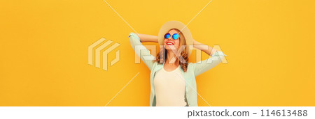 Happy relaxed young woman enjoying sunny warm day wearing summer straw hat on yellow background 114613488