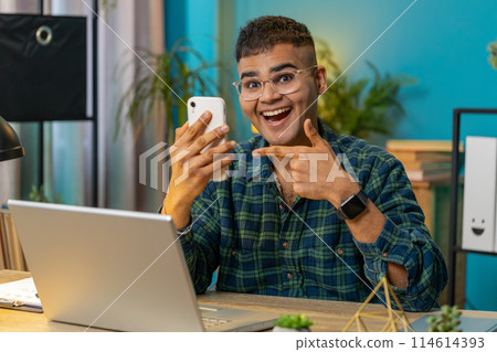 Smiling young businessman using smartphone online application pointing showing like thumbs up Smiling young businessman using smartphone online application pointing showing like thumbs up 114614393