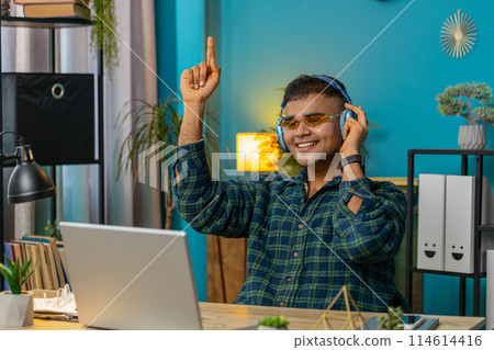 Overjoyed Indian man working on laptop celebrate success win money in lottery get online good news Overjoyed Indian man working on laptop celebrate success win money in lottery get online good news 114614416