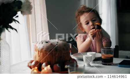 Little girl plays with homemade chocolate egg at the table decorated for Easter 114614961