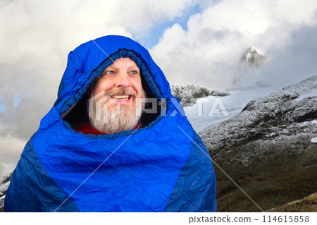 Happy bearded man in a sleeping bag against the backdrop of nature in the mountains 114615858